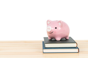 Pink piggy bank on top of books on wooden desk on white background, concept saving for education...