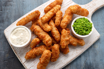Battered Haddock fish, mini fingers with mashed peas, tartar sauce on white wooden board