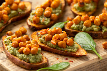 Sweet potato toast loaded with avocado guacamole and baked chickpeas sprinkled with chili flakes served on wooden board