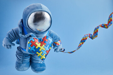 World Autism awareness day background. Blue plush astronaut toy with puzzle heart, autism symbol,...