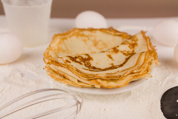 beautiful round thin pancakes on the kitchen table with flour and whisk and eggs