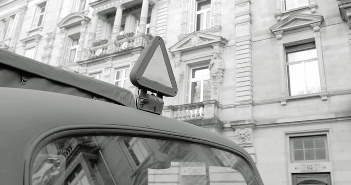 Triangle signage on the rooftop of a German 3-Ton Cargo Truck the workhorse of the German Army during WWII with typical Neustadt architecture in the background windows and balconies 4K DCI - black an