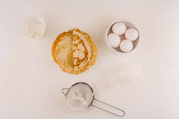 thin round pancakes with chicken eggs and flour on a white plate fried