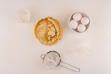 thin round pancakes with chicken eggs and flour on a white plate fried