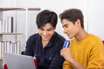 Happy Asian homosexual gay couple sitting together shopping online and holding credit card, LGBT family and e-commerce concept.