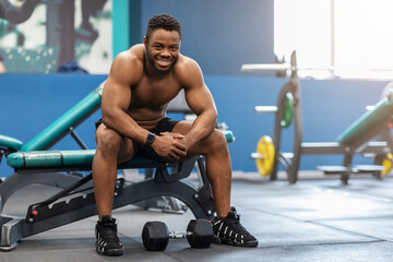 Obraz na płótnie Canvas Cheerful black guy resting after biceps work out, gym interior