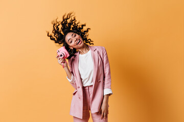 Emotional mixed race girl dancing on yellow background. Studio shot of excited woman with camera.