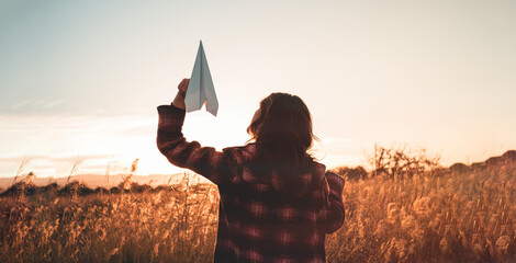 Giovane ragazza tiene in mano un aeroplano di carta. Vista di un campo al tramonto. 