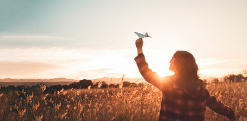 Travelling woman with paper airplane enjoying life and freedom at the land at sunset. Arms outstretched and happiness