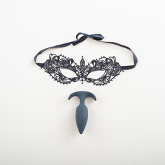 Black butt plug and lace mask on white background.