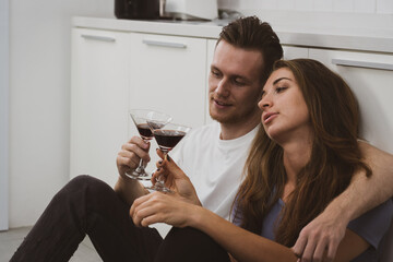 authentic picture of young caucasian couple sitting in the kitchen together and drinking wine for lunch in anniversary day