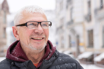 Portrait of smiling mature man spectacled against backdrop of beautiful urban houses in winterr