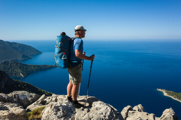 Hiking on Lycian way. Man with backpack standing on rock cliff high above Mediterranean sea enjoying the view, Trekking in Turkey on Lycian Way trail, outdoor activity