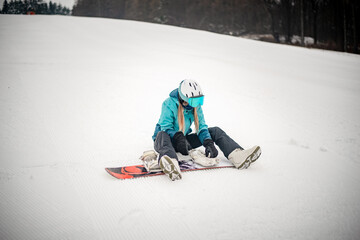 Blonde woman wearing black and blue outfit is getting her snowboard binding ready