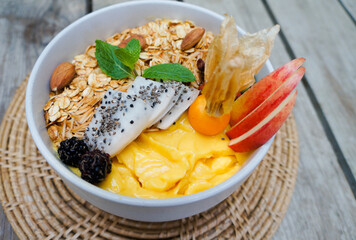 Close up Mango smoothie bowl with granola, seeds , almond fresh apple in White ceramic bowl.detox, vegetarian  food concept on table