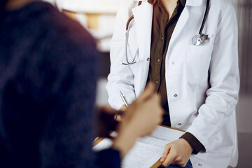 Doctor and patient discussing current health examination while sitting in sunny clinic. Medicine...