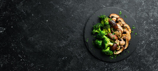 Organic food. Fried mushrooms and broccoli on a black stone plate. Rustic style. Top view.