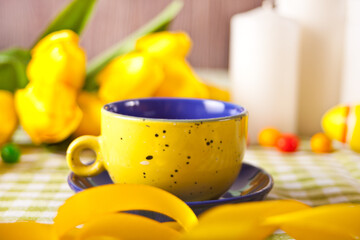 Easter spring table with yellow cup, yellow tulips and candles on the background.