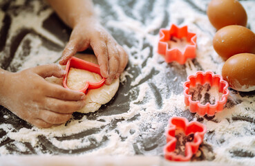 Close up of kid hands carving dough with cookie cutters. Easter baking preparation. Cookies for Christmas. 