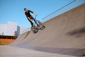 Male bmx rider doing trick on ramp in skatepark