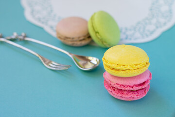 French macarons or macaroons close up on blue background with white ornamental napkin and dessert spoon and fork. Colorful almond round meringue biscuit with different interlayers