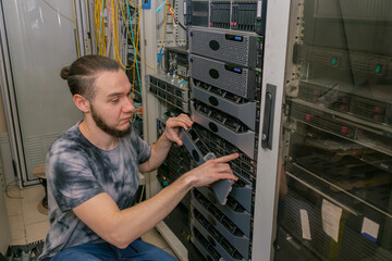 A young man works in a server room. A technician maintains computer equipment in a data center. An...