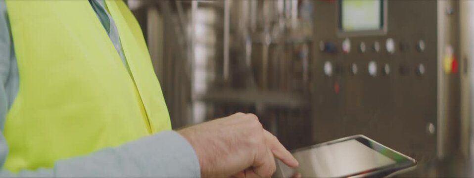 Tilt down shot of mature engineer wearing protective face mask and swiping with fingers on digital tablet screen. Using wireless devices in production process control concept.