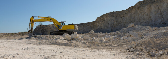 A large yellow tracked excavator is mining rock in a quarry.