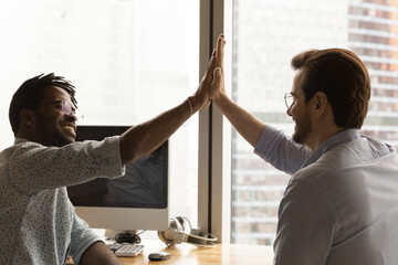 Give me five. Diverse colleagues black and caucasian managers employees join hands high celebrate common achievement. Two young men successful teammates friends greet each other with great job result