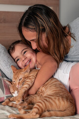 Mother, daughter and their cat, playing on the bed at home.