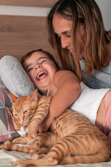 Mother, daughter and their cat, playing on the bed at home.