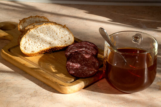 A cup of tea with bread and kalbasa on a wooden board.