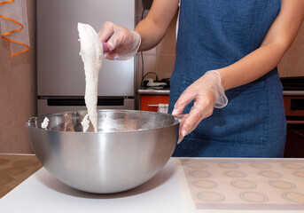 The girl is holding a spatula, mixing the dough for macaroons in a metal bowl.