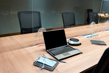 Laptop display blank and face shield ,mask on table in meeting room with clear acrylic sheet separates the center on the conference table to prevent COVID-19