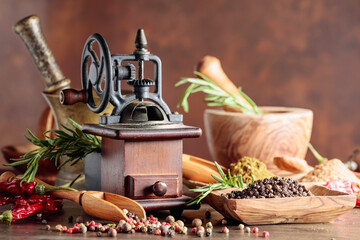 Vintage pepper mill with kitchen utensils, spices and rosemary on a old wooden table.