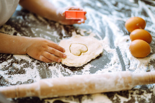 Close up of boy hands carving dough with cookie heart cutters. Easter baking preparation. A little chef carves ginger Cookies.