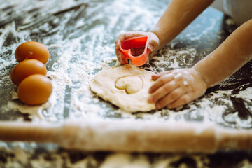 Close up of boy hands carving dough with cookie heart cutters. Easter baking preparation. A little chef carves ginger Cookies.