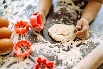 Close up of boy hands carving dough with cookie heart cutters. Easter baking preparation. A little chef carves ginger Cookies.