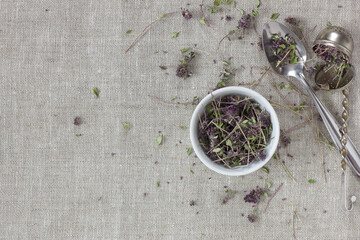 Thyme dried flower tea in a white bowl on linen textile with blossoms and spoon nearby, closeup,...