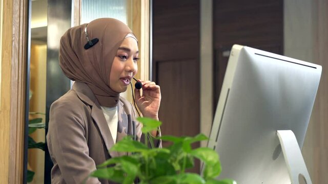 Beautiful Asian Muslim women wearing hijab working in call center office, Confident Islam woman worker in Customer Support smiling joyful to Support Customers