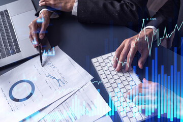 Two traders man and woman researching historic data to predict stock market behavior. Internet trading concept. Forex and financial hologram chart over the table with the documents