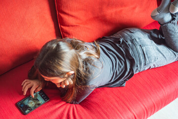 Young girl 10 years old is using smartphone on the sofa. Lifestyle, indoors. 