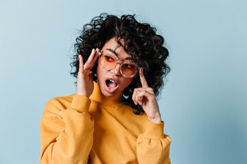 Amazed curly woman posing in sunglasses. Studio shot of emotional mixed race girl expressing...