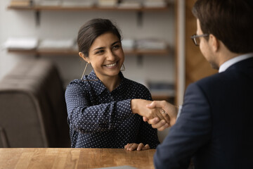 Greetings, you are hired. Happy young indian female successful job seeker shake hand of male hr...