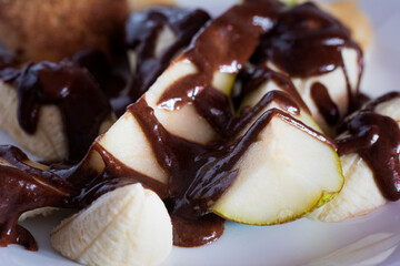 Banana pear dessert on white plate poured with chocolate. Vegetarian salad.