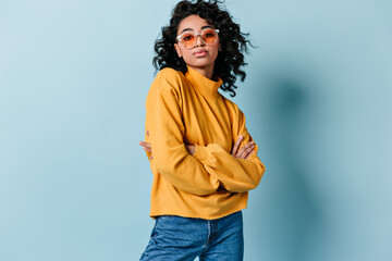 Serious curly woman posing with crossed arms. Studio shot of brunette girl in yellow sweatshirt.