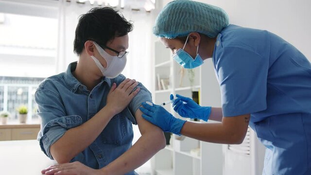Young Asia lady nurse giving Covid-19 or flu antivirus vaccine shot to senior male patient wear face mask protection from virus disease at health clinic or hospital office. Vaccination concept. - Powered by Adobe