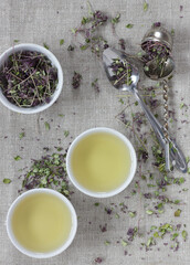 Thyme dried flower herbal tea in a white chinese cups on linen textile with blossoms and spoon nearby, closeup, copy space, flat lay, from above overhead top view, healthy herbal teas concept