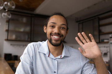 Portrait of positive young black guy look at digital web camera make video call wave hand welcome...