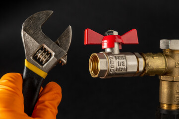 Hand in glove holds an adjustable wrench on the background of plumbing tap. Concept of plumbing...